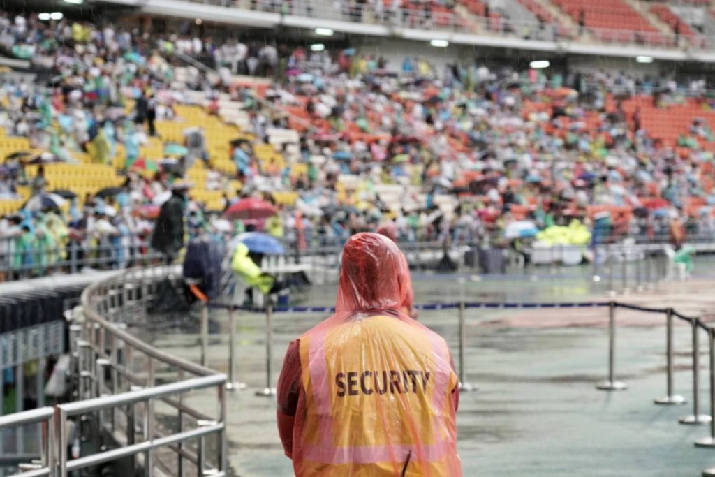 ผู้รักษาความปลอดภัยใส่เสื้อกันฝนยืนคุ้มพื้นที่ที่ราชมังคลากีฬาสถาน